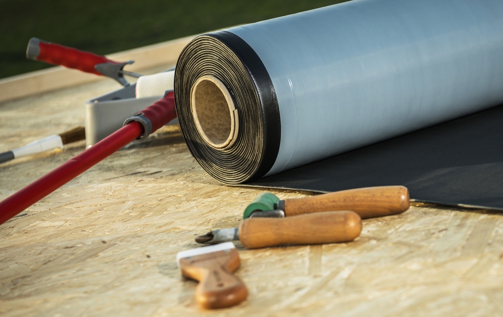 Roll of modern EPDM roofing rubber material alongside some tools
