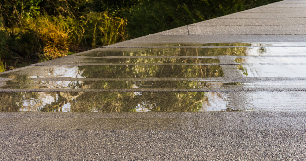 Close-up of a construction defect on a flat roof with a puddle of water
