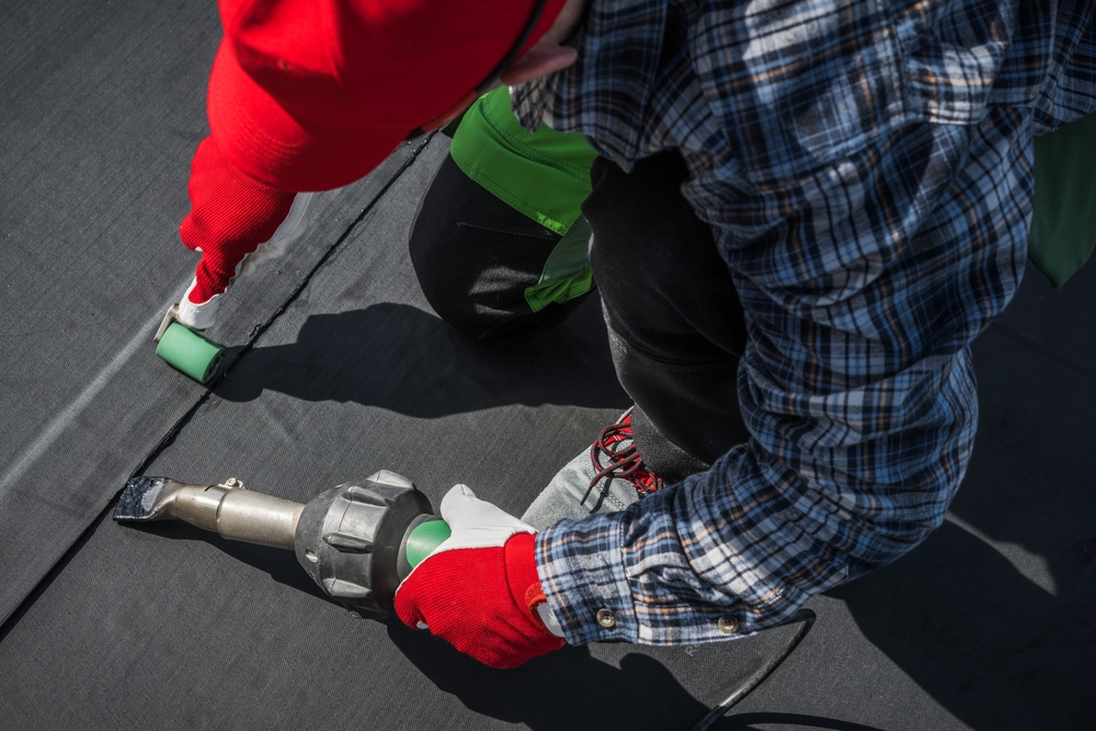 Roofing worker using a hot air blower for EPDM roof membrane rubber installation
